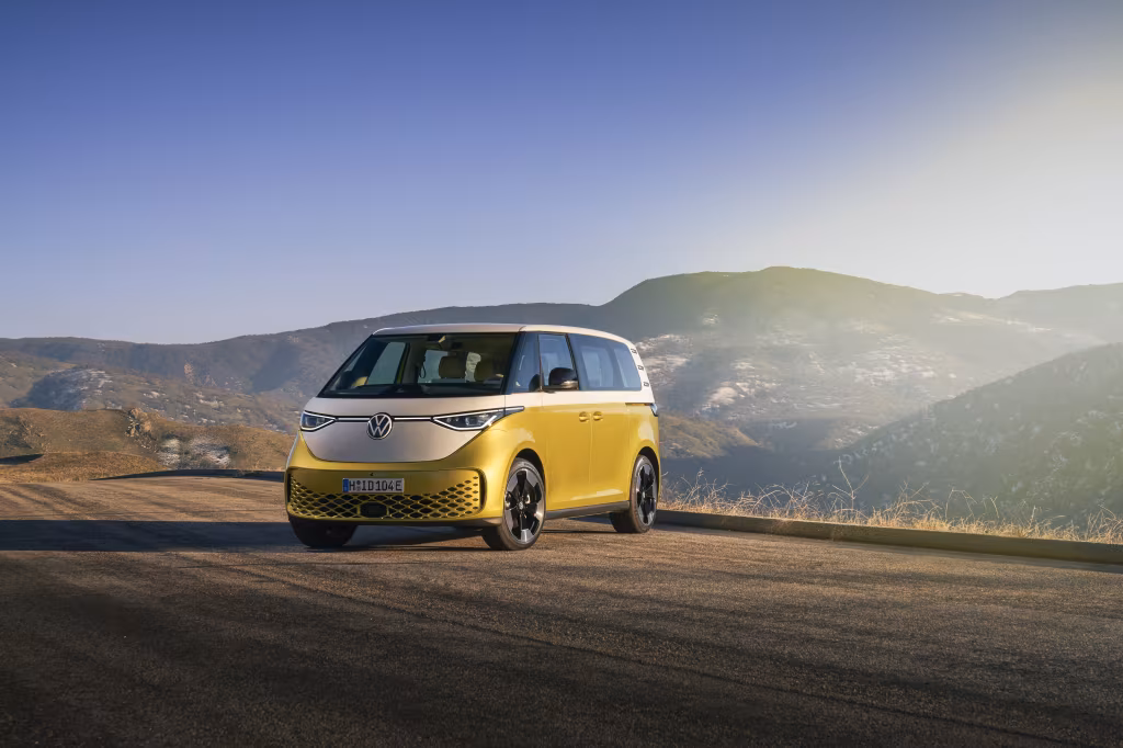Volkswagen ID. Buzz припаркован на горной дороге на фоне холмов и заката.